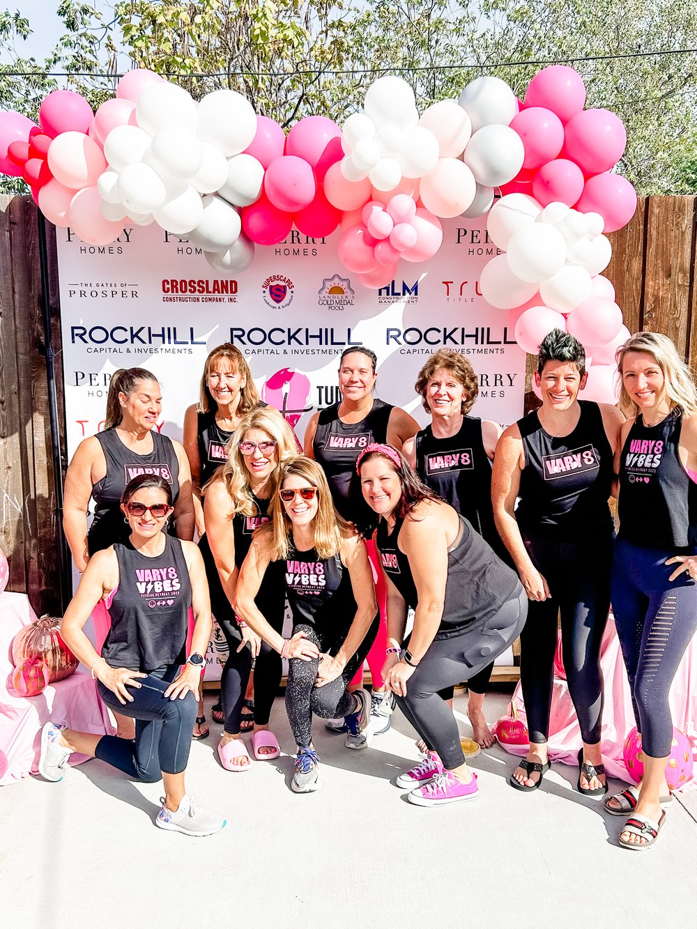 Vary-8 women at race day in matching tanks under a balloon arch